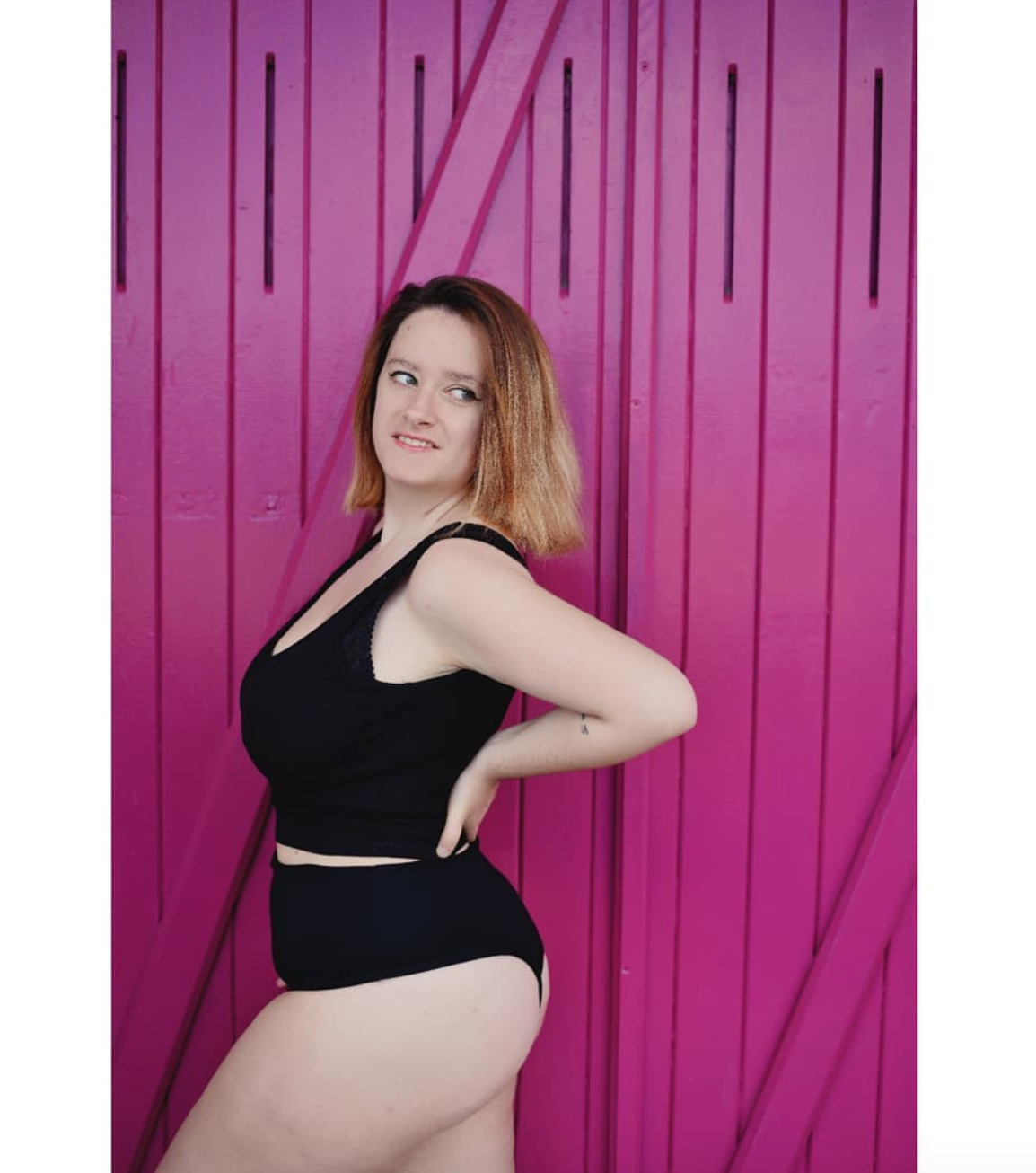 photo sur fond rose de l'influenceuse bodypositive @elenacurvymodel portant un top noir et une culotte muse underwear noire de profil