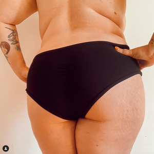 gros plan sur les fesses d'une femme ronde les mains sur les hanches portant un shorty noir de la marque muse underwear