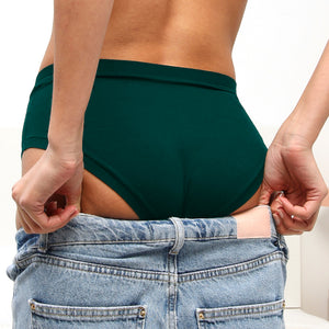 Gros plan sur une femme de dos en slip vert foncé en train d'enfiler son jeans